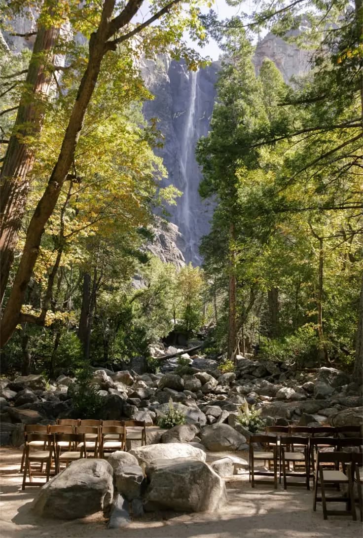 A wedding ceremony set with wooden chairs and florals beneath a national park waterfall